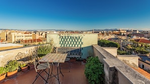 Eine Dachterrasse mit Tisch und Stühlen, Blumentöpfen und Blick auf die Stadtlandschaft.