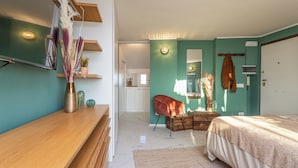 Ein Schlafzimmer mit einem Bett, einem Fernseher, einer Holzkommode, einem Stuhl und einem Schreibtisch mit Blumen in einer Vase.
