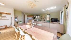 Ein modernes Wohnzimmer mit einem großen Holzesstisch, weißen Stühlen, einer Couch und einem Fernseher.