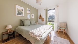 Ein Schlafzimmer mit Bett, Nachttisch, Lampe und Blick ins Freie.