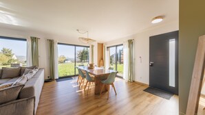 Ein modernes Wohnzimmer mit Holzesstisch, hellen Sofas und großen Fenstern mit Blick ins Freie.