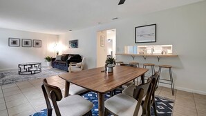 A modern dining area with a wooden table and chairs, a ceiling fan, and a kitchen area with bar stools.