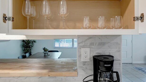 A kitchen with a marble countertop, a coffee maker, and a cabinet with white plates and glasses.