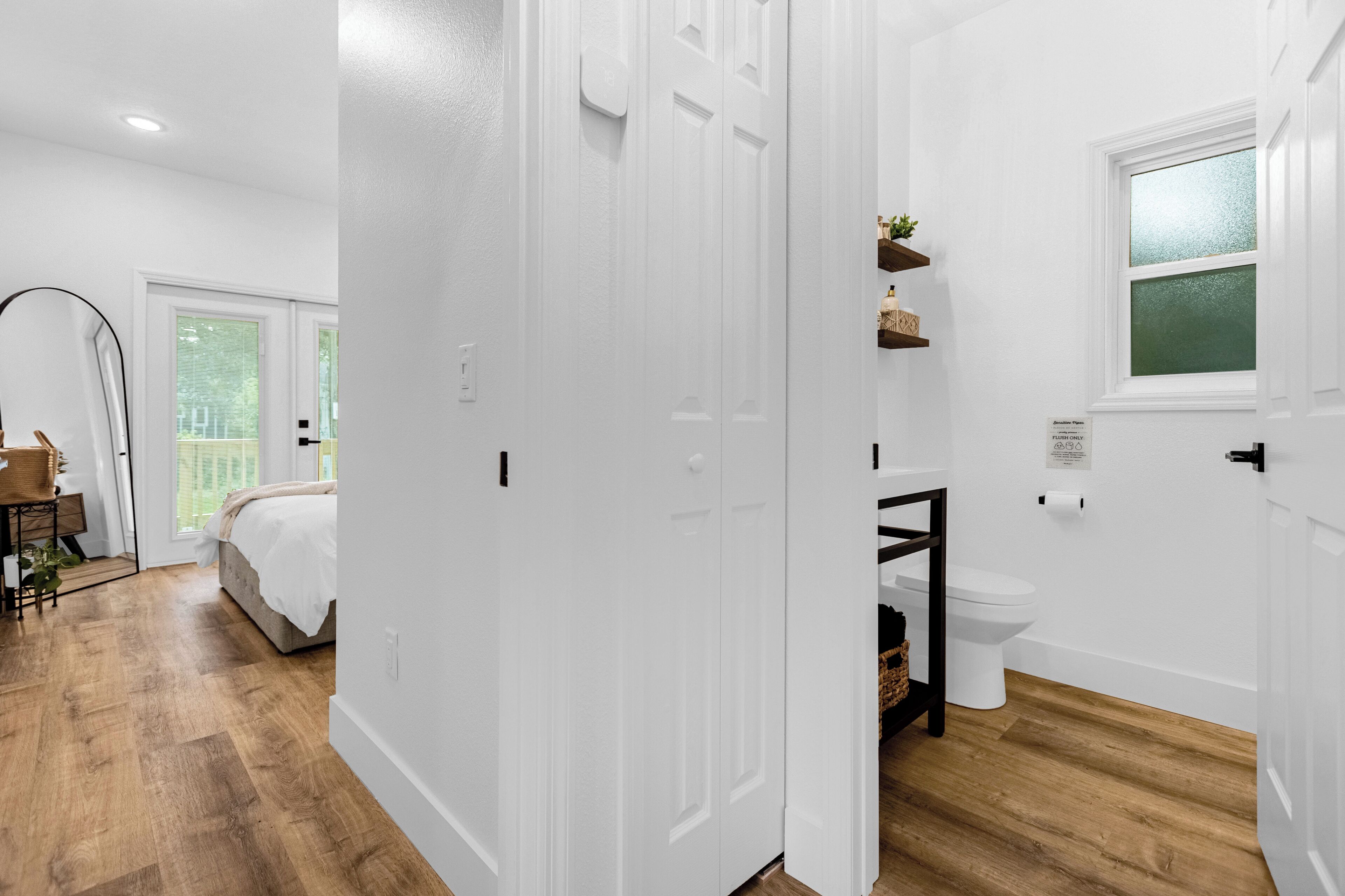 A modern bathroom with white walls, a wooden floor, a toilet, and a window.