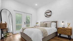 A bedroom with a large bed, a nightstand, a mirror, and a window with blinds. - Treehouse Lake Davis - 1BR Private Modern Home with Balcony Downtown (Orlando)