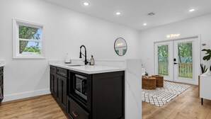 A modern kitchen with a black and white color scheme, a large island, and a view of the outdoors through a glass door. - Treehouse Lake Davis - 1BR Private Modern Home with Balcony Downtown (Orlando)