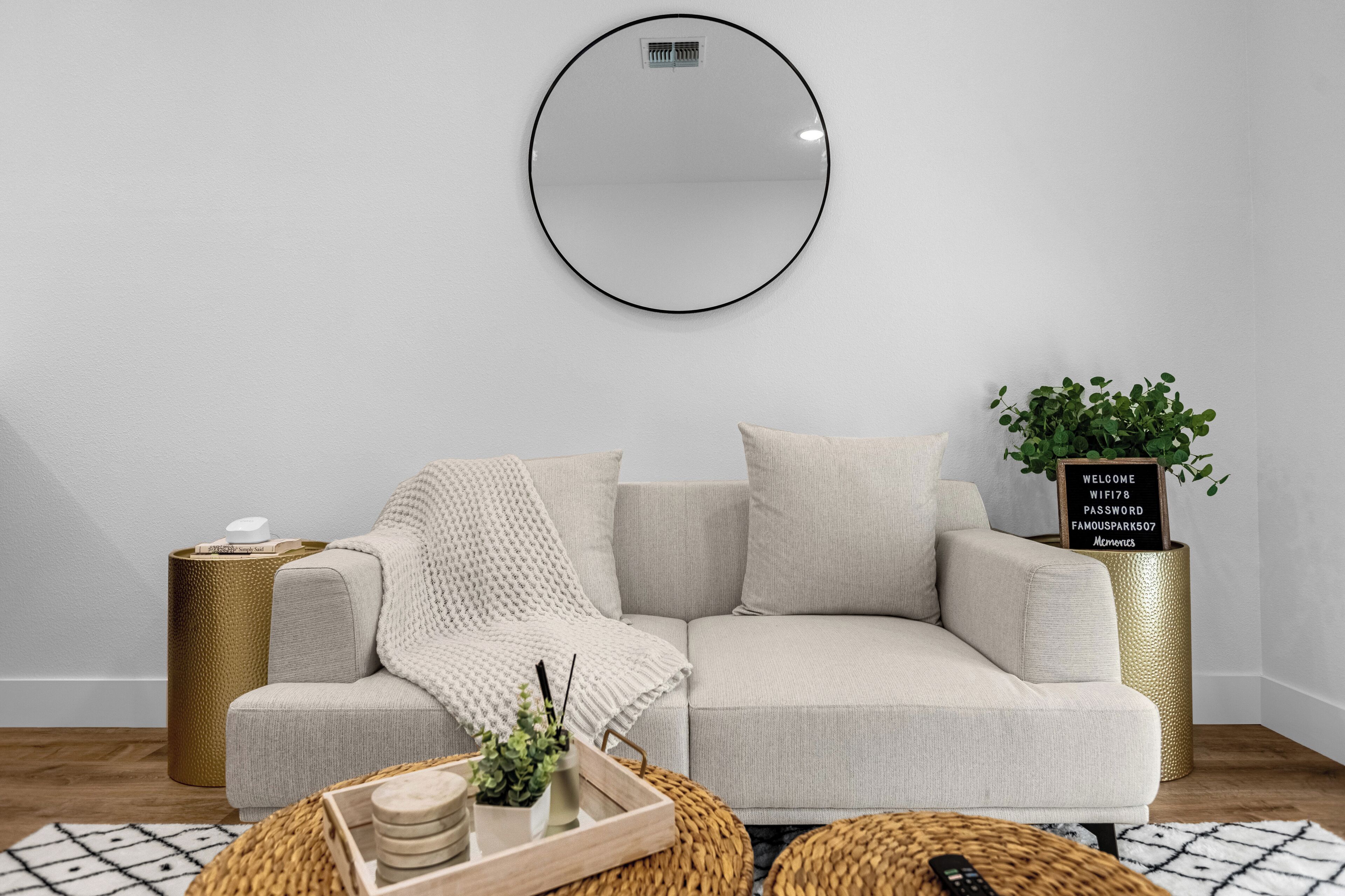 A modern living room with a beige sofa, a round mirror, a small plant, and a tray with decorative items.