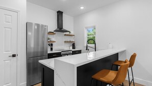 A modern kitchen with a stainless steel refrigerator, black cabinetry, a marble countertop island, and two brown bar stools. - Treehouse Lake Davis - 1BR Private Modern Home with Balcony Downtown (Orlando)