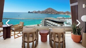Un balcón con sillas de mimbre y una pequeña mesa, con vistas a una playa y un paisaje montañoso.