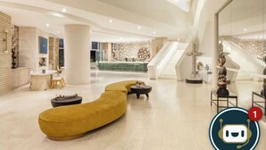 Un vestíbulo amplio con diseño moderno, que cuenta con un sofá amarillo curvo, una escalera y una zona de recepción.