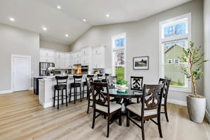 A modern kitchen with white cabinets, a dining area with a glass table, and a potted plant.