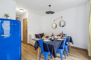 Un espace de vie compact comprenant un coin repas, un réfrigérateur bleu et un lit doté d’une porte en bois.
