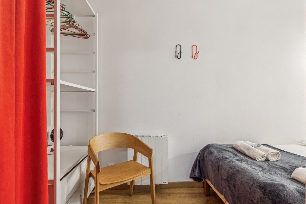 A bedroom with a wooden chair, a bed with a grey blanket, and a white radiator.