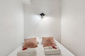 A spa room with two beds, each with a fluffy pillow and a towel. A modern light fixture is mounted on the wall above the beds. - Lavie Maison Cozy 3BR Haven w Parking (Bordeaux)