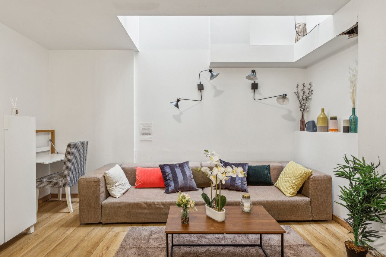 Un salon moderne avec un canapé marron, une table basse et un coin repas avec une chaise. On y trouve également des plantes décoratives et des luminaires fixés au mur.
