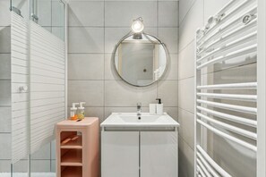 Une salle de bain moderne avec un miroir rond, un lavabo blanc et un porte-serviettes.