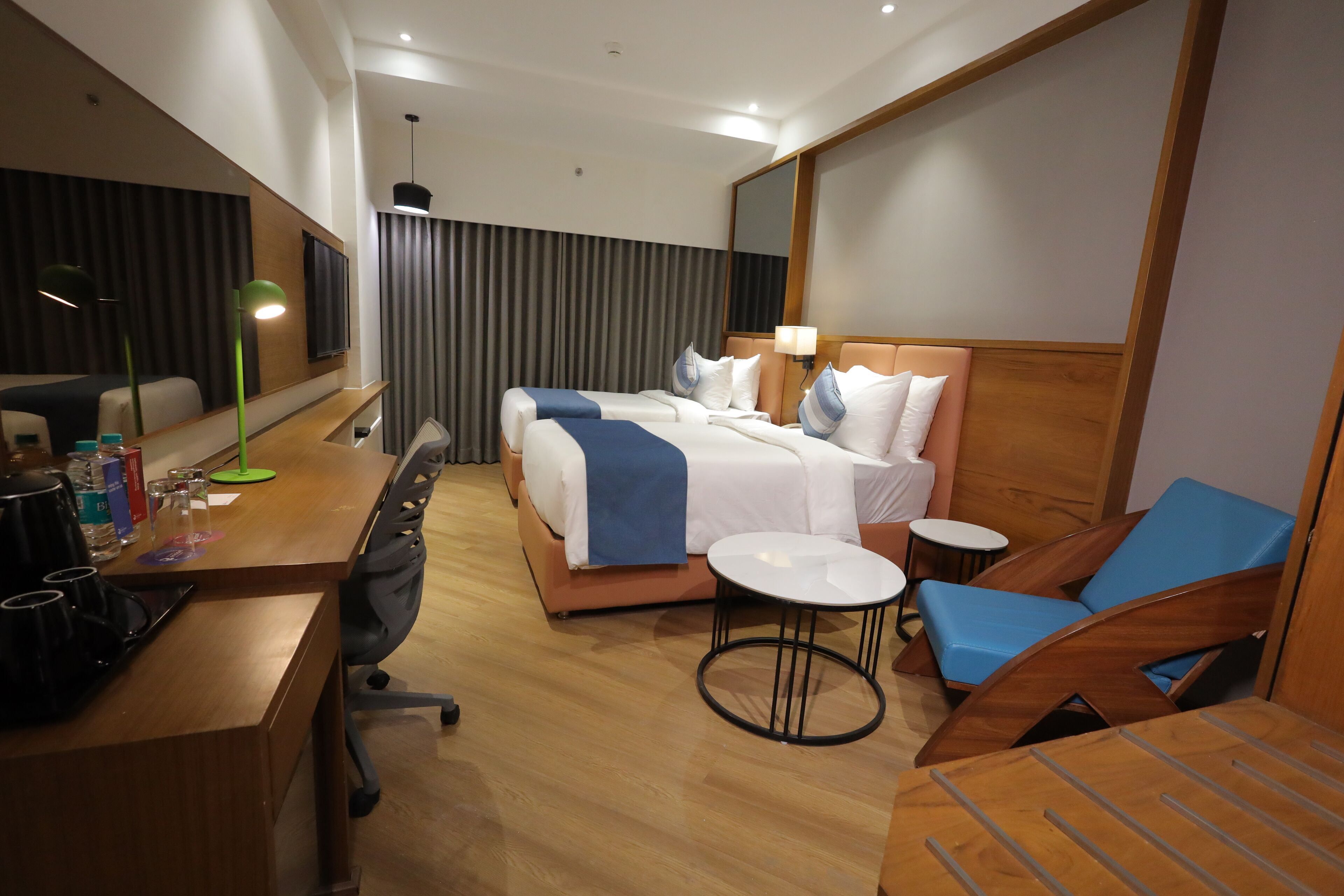 Una habitación de hotel con cama, mesitas de noche, escritorio, silla, una pequeña mesa redonda y un espejo.