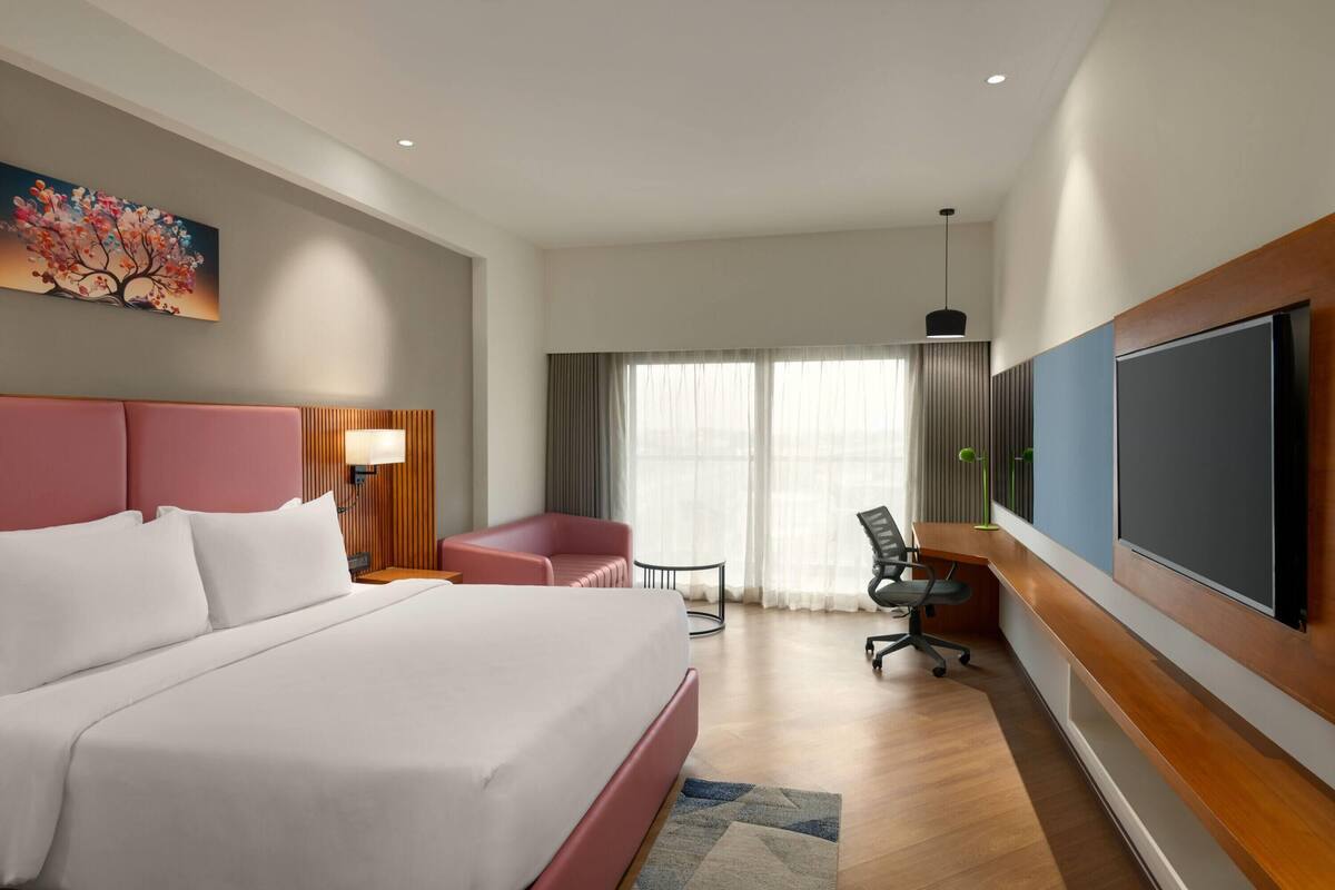 A hotel room with a large bed, a desk, a chair, a TV, and a painting on the wall.