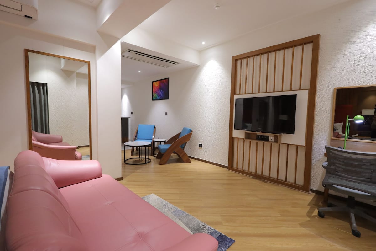 A modern living room with a pink sofa, blue chairs, a TV, and a wooden partition.