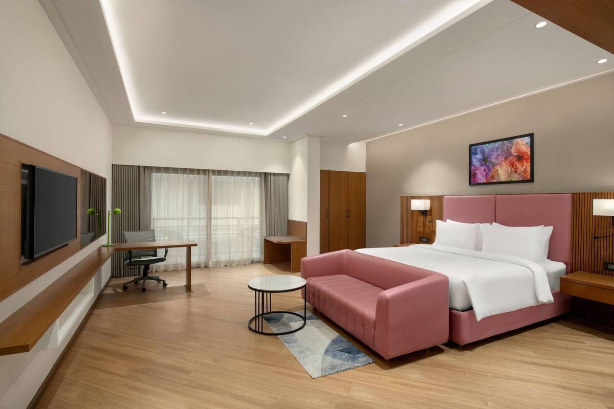 A modern hotel room with a large bed, a desk, a chair, and a television.