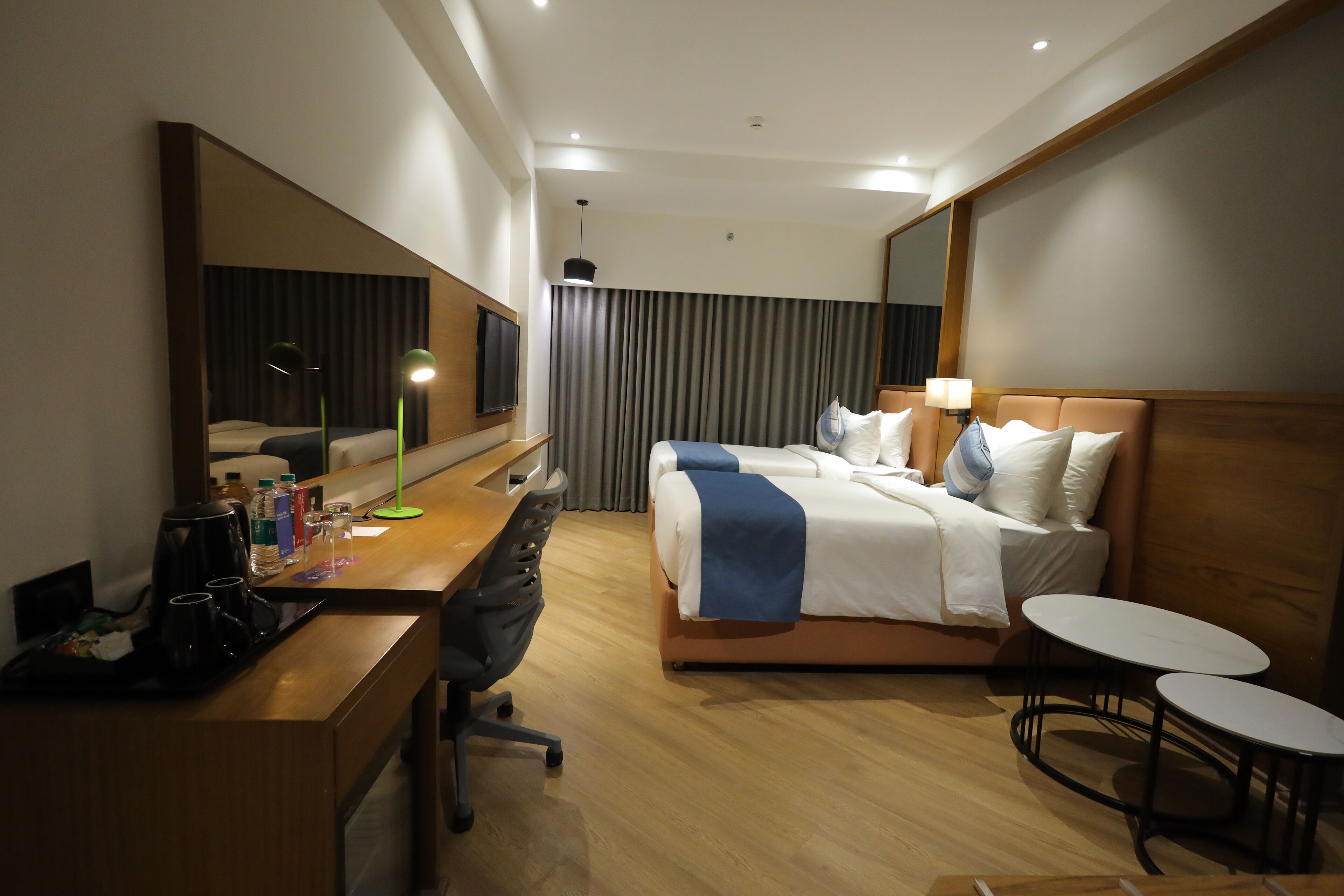 A hotel room with a bed, bedside tables, a desk with a chair, a coffee maker, and a TV.