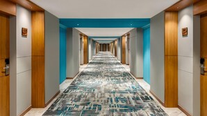 A hotel hallway with a patterned carpet, wooden doors, and a blue accent wall. - Ramada Encore By Wyndham Viramgam (Viramgam)