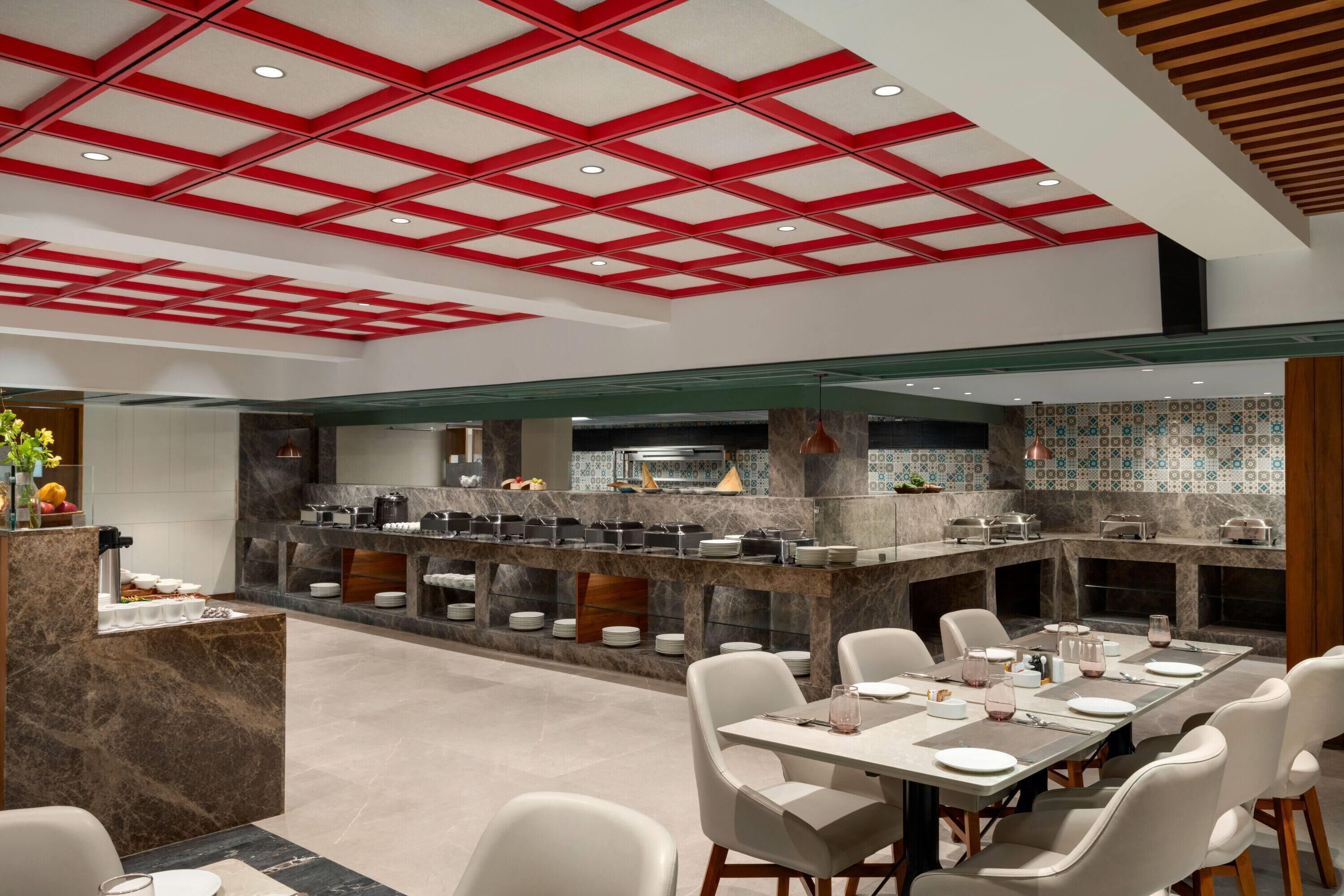 Een modern restaurant met een centraal eiland, witte stoelen en een rood plafondontwerp.