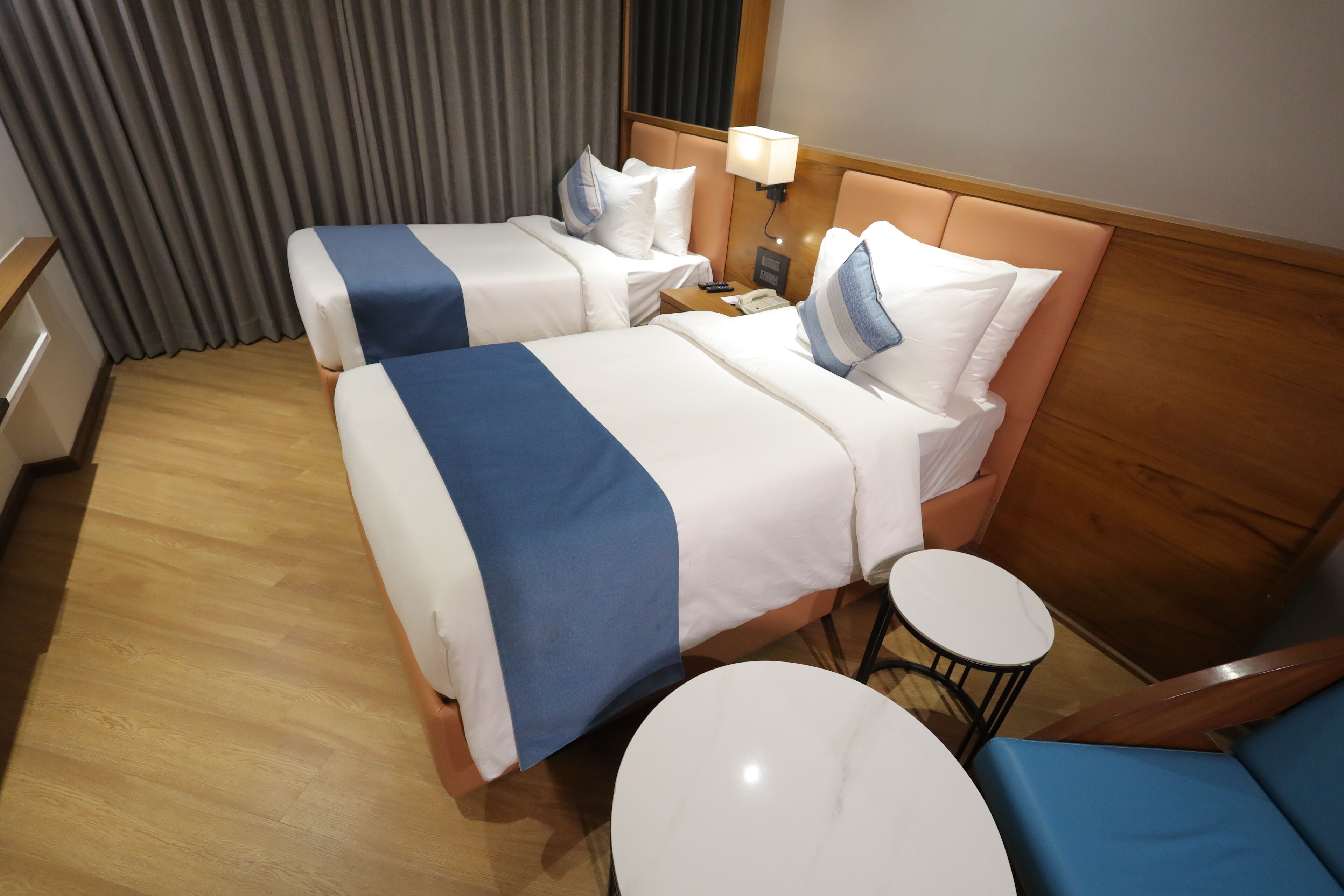 A hotel room with two beds, a small round table, a chair, and a nightstand with a lamp.