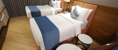 A hotel room with two beds, a small round table, a chair, and a nightstand with a lamp.