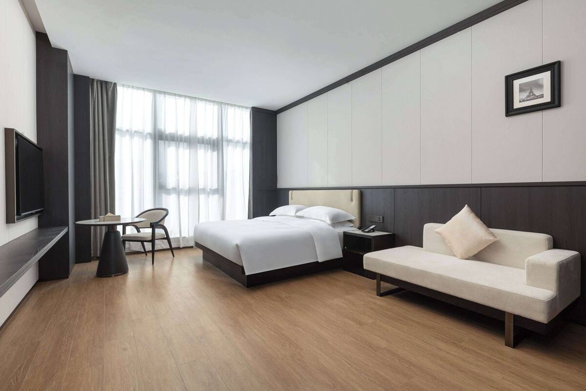 A modern hotel room with a bed, a sofa, a desk, and a TV.