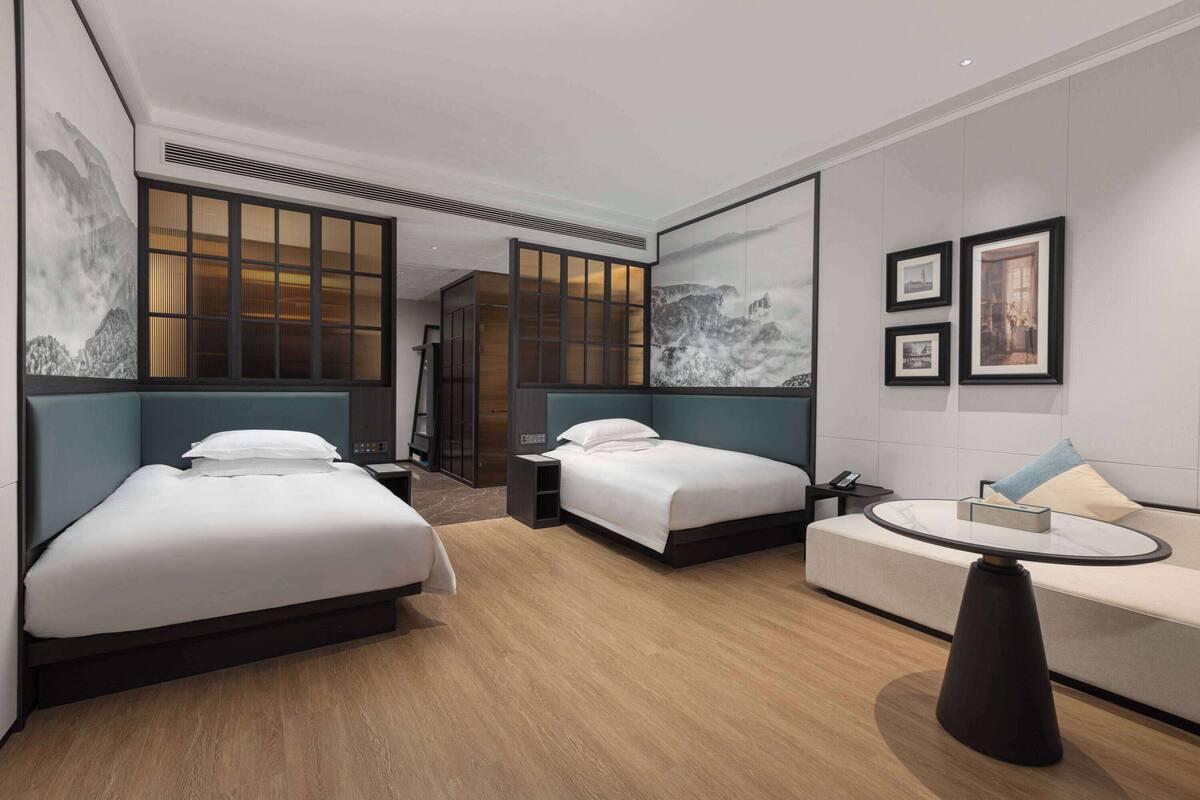 A hotel room with two beds, a sofa, a round table, and artwork on the walls.