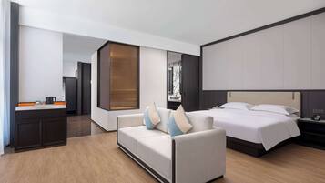 Una habitación de hotel moderna con sofá, cama, mesita de noche, escritorio con hervidor y un espejo grande.