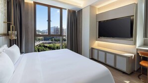 Ein Hotelzimmer mit einem großen Bett, einem an der Wand befestigten Fernseher und Blick auf die Stadt.