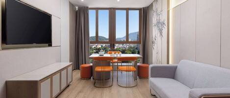 A modern living room with a flat-screen TV, a dining area with orange chairs, and a grey sofa.