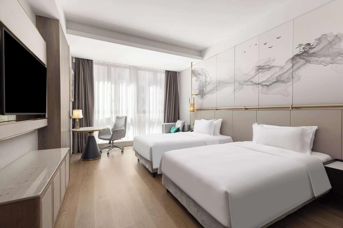 A hotel room with two beds, a desk, a chair, and a large wall mural.