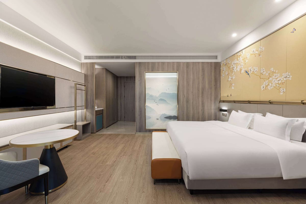 A modern hotel room with a large bed, a flat-screen TV, a dining area, and a wall with a floral mural.