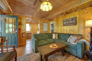 Un intérieur en bois avec un canapé vert, une table basse en bois et un panneau d’accueil.