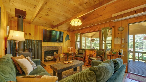 Ein gemütliches Blockhaus-Interieur mit einem grünen Sofa, einem Kamin, Holzwänden und einem Fernseher.