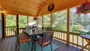Eine überdachte Terrasse im Freien mit Tisch und Stühlen, großen Fenstern und einem hängenden Blumenkorb.