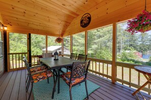 Une terrasse extérieure couverte, dotée d’une table et de chaises, de grandes fenêtres et d’une jardinière suspendue.