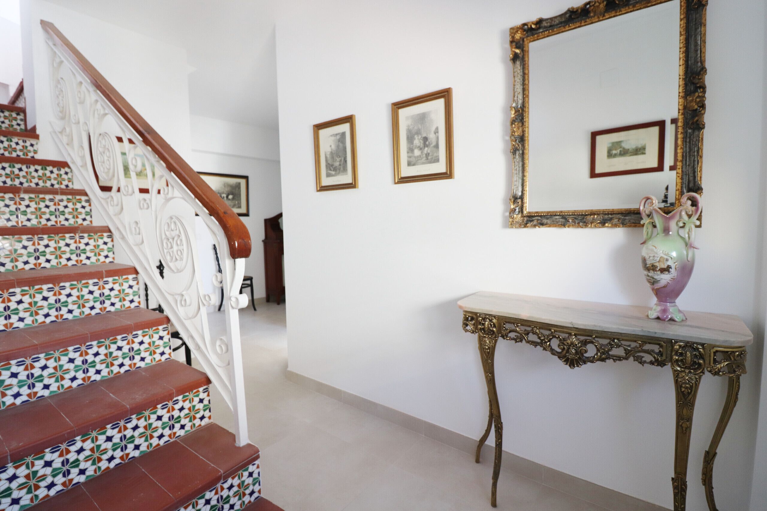 Una escalera con baldosas estampadas, una consola con un florero y cuadros en la pared.