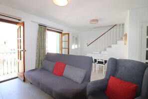 Ein Wohnzimmer mit grauem Sofa und Sessel, einer Treppe und einem Essbereich.