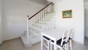 A white staircase with a wooden handrail leading to a landing. A white dining table with four chairs is positioned on the landing. - 1002 Casa Miramar (Nerja)