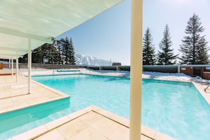 A swimming pool with a view of snow-covered mountains and tall evergreen trees.