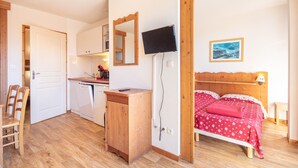 A compact bedroom with a wooden bed, a small bedside table, a mirror, and a TV mounted on the wall. - L'Etoile des Neiges - Station de ski à pied (Chamrousse)