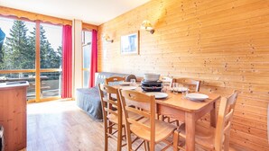 A wooden interior with a dining table, chairs, and a view of trees through large windows. - L'Etoile des Neiges - Station de ski à pied (Chamrousse)