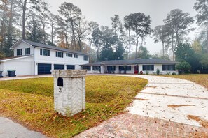 Stroll up the brick pathway to a charming two-story home with a garage, nestled among tall trees.