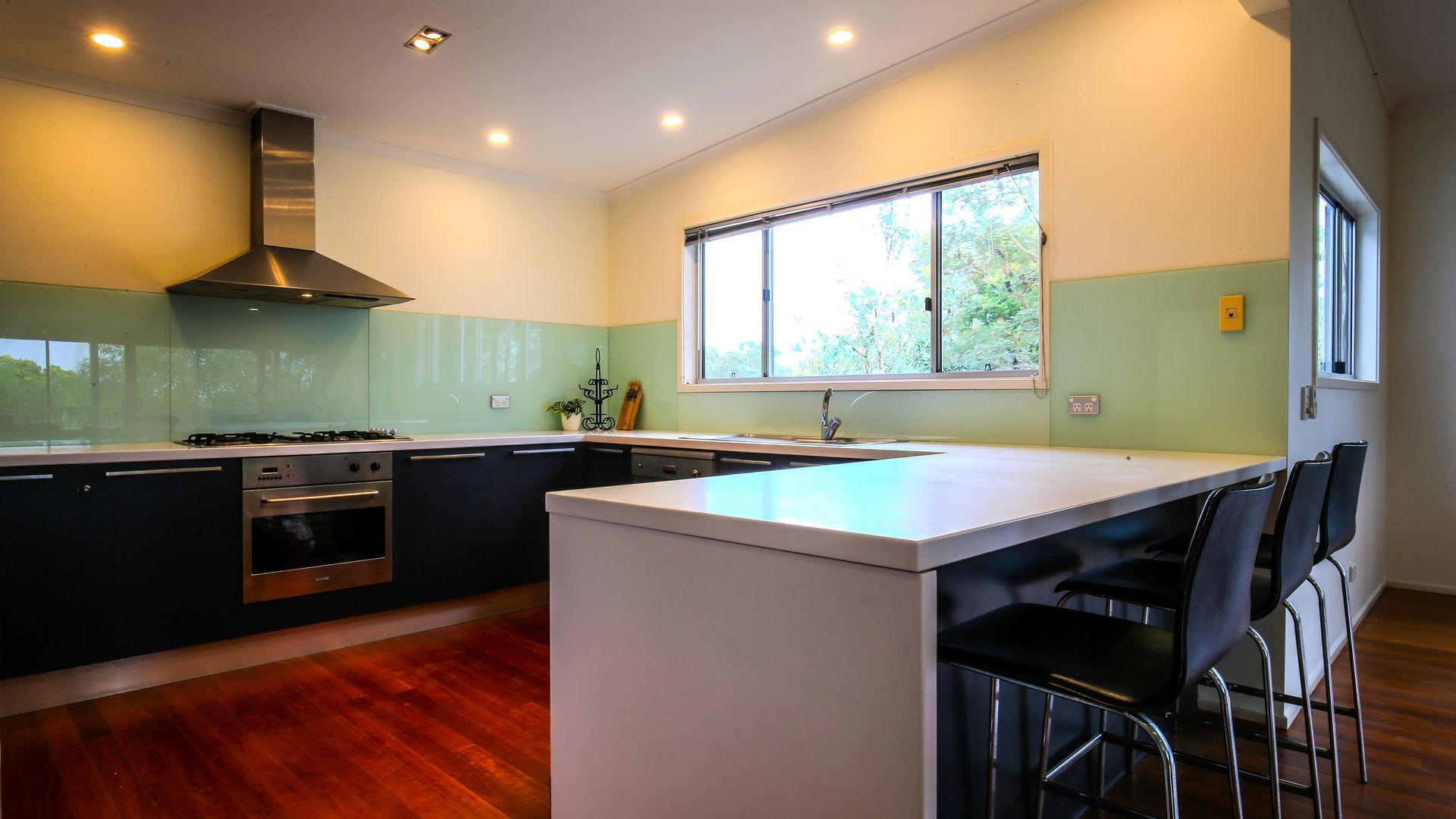 A modern kitchen with a central island, stainless steel appliances, and a large window providing natural light.