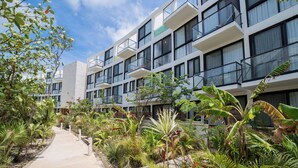 A modern hotel with multiple balconies, a central courtyard with tropical plants, and a clear sky. - Wellness Suite with Spa, Gym & Rooftop (Tulum)