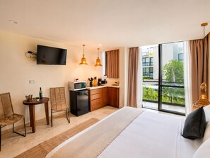 A hotel room with a bed, a kitchenette, a dining area, and a large window offering a view of the outdoors. - Wellness Suite with Spa, Gym & Rooftop (Tulum)